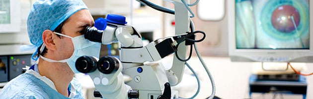 doctor in scrubs with mouth cover in office staring into microscope